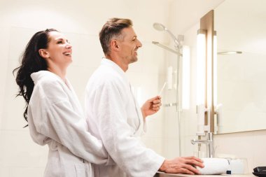 Otelde gülümseyen kız arkadaşın diş fırçasıyla sevgilisine sarılışının yan görüntüsü. 