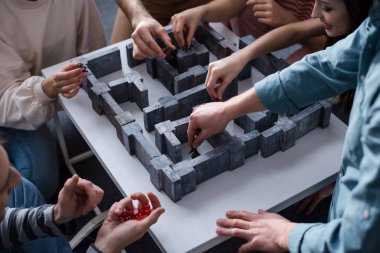 KYIV, UKRAINE - JANUARY 27, 2020: cropped view of young friends playing labyrinth board game at home clipart