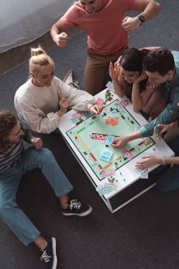 KYIV, UKRAINE - JANUARY 27, 2020: overhead view of excited man showing winner gesture while playing monopoly game with cheerful friends  clipart