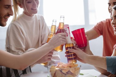 Bira şişeleri ve plastik bardakları sodayla tokuşturan mutlu arkadaşların kırpılmış görüntüsü. 