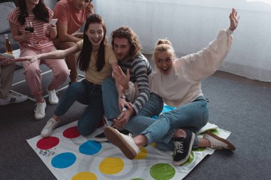 KYIV, UKRAINE - JANUARY 27, 2020: high angle view of friends sitting on twister game mat while others resting on sofa clipart