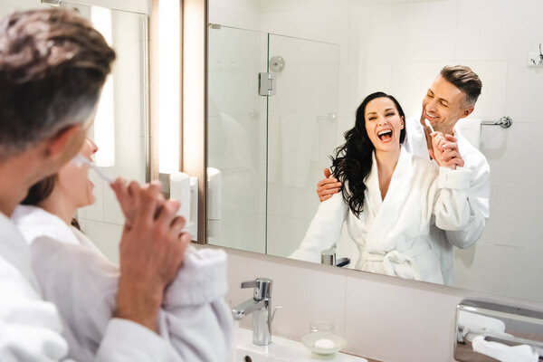 избирательное внимание парня обнимающего улыбающуюся подружку с зубной щеткой в отеле
