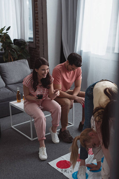 KYIV, UKRAINE - JANUARY 27, 2020: cheerful girl holding glass of red wine and pointing with finger at friends playing twister game