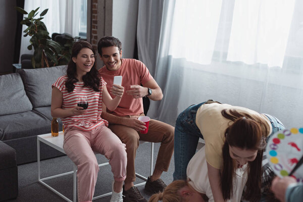 KYIV, UKRAINE - JANUARY 27, 2020: smiling girl taking photo of friends playing twister game