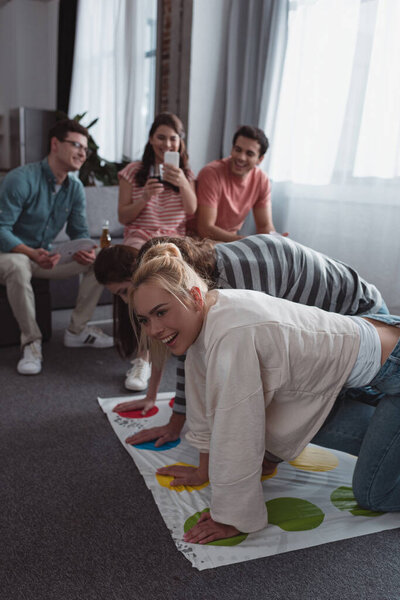 KYIV, UKRAINE - JANUARY 27, 2020: smiling girl taking photo of cheerful friends playing twister game 