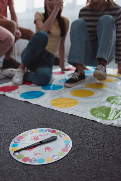 KYIV, UKRAINE - JANUARY 27, 2020: selective focus of moves plate near friends sitting on twister game mat