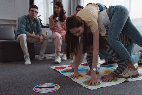 KYIV, UKRAINE - JANUARY 27, 2020: cheerful girls playing twister game while friends resting on sofa
