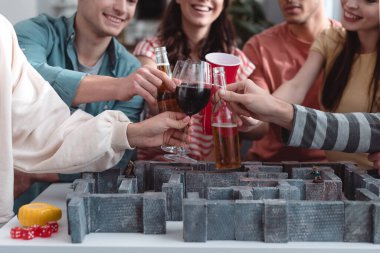 KYIV, UKRAINE - JANUARY 27, 2020: cropped view of cheerful friends with beer and wine near labyrinth game  clipart