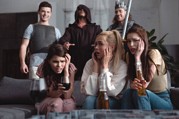 shocked girls drinking beer and wine while men in fairy characters costumes standing on background