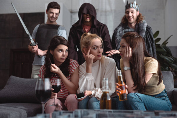selective focus of girls talking and drinking beer and wine and men in fairy characters costumes standing on background