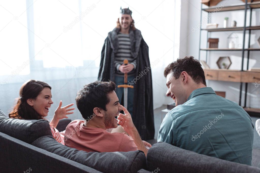 selective focus of smiling man in fairy king costume standing near laughing friends