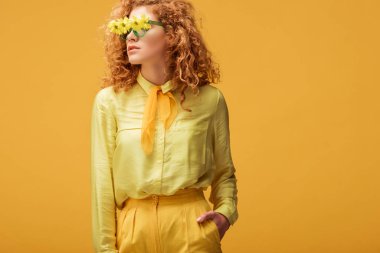 Güneş gözlüklü şık kızıl saçlı kadın, çiçekli, cebinde sarıda tek başına duran. 