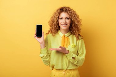 Sarı ekranda boş ekranlı akıllı telefonu işaret eden mutlu kızıl saçlı kadın. 