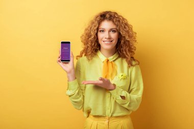 Kyiv, Ukrayna - 4 Şubat 2020: Sarı ekranda Instagram uygulamalı akıllı telefonu işaret eden mutlu kızıl kadın 