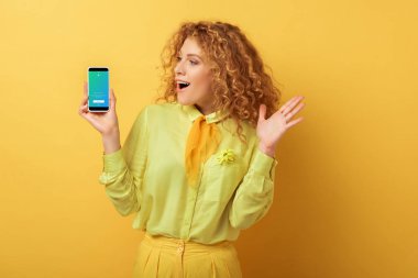 Kyiv, Ukrayna - 4 Şubat 2020: Sarı twitter uygulaması ile akıllı telefona bakan heyecanlı kızıl saçlı kadın 