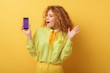 Kyiv, Ukrayna - 4 Şubat 2020: Sarı İnstagram uygulamalı akıllı telefona bakan heyecanlı kızıl saçlı kadın 