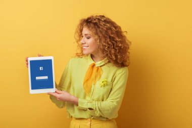 Kyiv, Ukrayna - 4 Şubat 2020: neşeli kızıl saçlı kadın elinde facebook uygulaması olan dijital tablet tutuyor. 