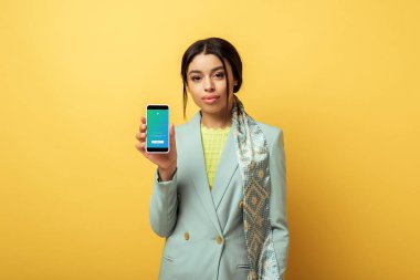 Kyiv, Ukrayna - 4 Şubat 2020: Güzel Afrikalı Amerikalı kız twitter uygulaması ile sarı renkli akıllı telefon tutuyor. 