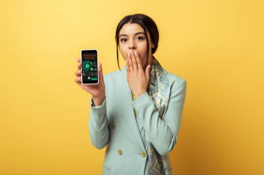 Şok olmuş Afrikalı Amerikalı kız yüzünü örtüyor ve elinde sarı pazarlama analiziyle akıllı telefon tutuyor. 