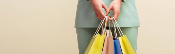 panoramic shot of young woman holding shopping bags isolated on beige 