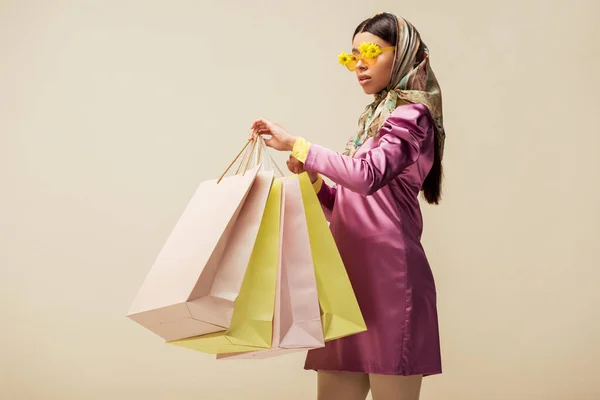 아름다운 아프리카계 여자가 선글라스를 스카프를 착용하고 베이지에 고립된 쇼핑백을 — 스톡 사진