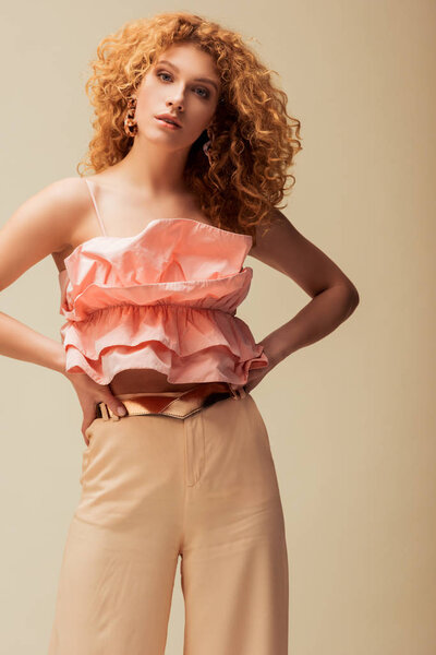 attractive redhead woman standing with hands on hips isolated on beige 