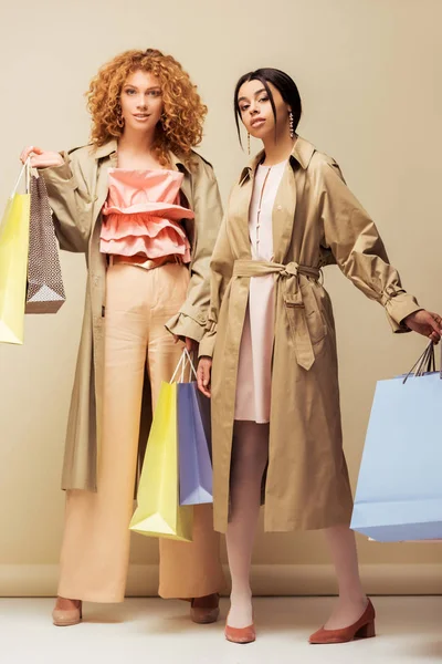 Beautiful Multicultural Girls Trench Coats Standing Shopping Bags Beige — Stock Photo, Image