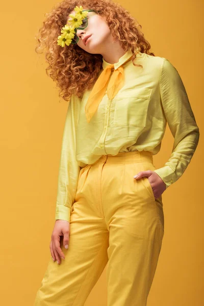 戴太阳镜的红头发卷曲女人 双手插在口袋里 与黄色隔离 — 图库照片