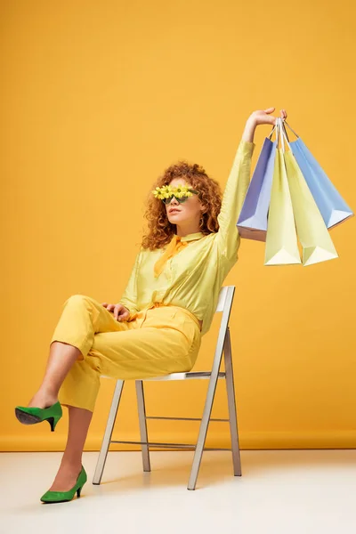 Стильна Руда Жінка Сонцезахисних Окулярах Квітами Тримає Сумки Сидячи Жовтому — стокове фото