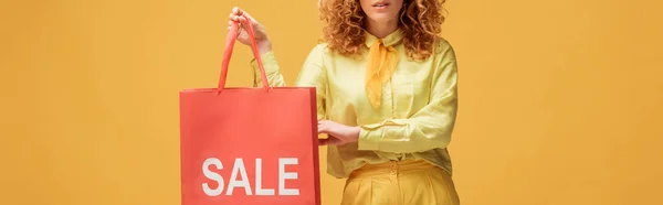黄色に単離された販売レタリングで買い物袋を保持スタイリッシュな赤毛の女性のパノラマショット — ストック写真