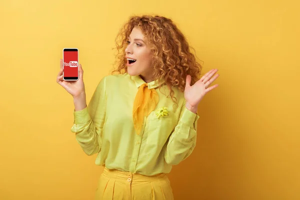 Kyiv ウクライナ 2020年2月4日 興奮した赤毛の女性は黄色の上にYoutubeアプリでスマートフォンを見て — ストック写真