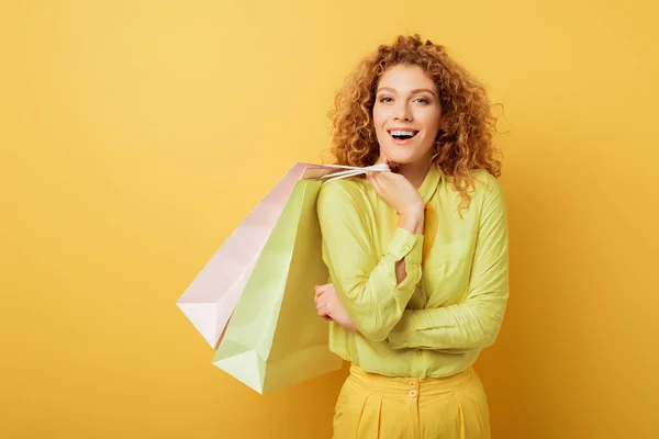 Nachdenkliche Und Lockige Frau Mit Einkaufstüten Auf Gelbem Grund — Stockfoto
