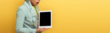 Panoramik çekim, şok olmuş Afro-Amerikan kadının elinde dijital tablet ve sarı ekranda izole edilmiş beyaz ekran. 