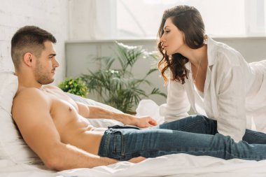Beyaz gömlekli seksi kız. Gömleksiz erkek arkadaşına bakıyor. Yatakta kot pantolonla yatıyor.