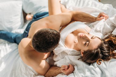 Seçici odak noktası, üstsüz genç bir adamın seksi kız arkadaşını kucaklaması. Yatakta gözleri kapalı yatıyor.