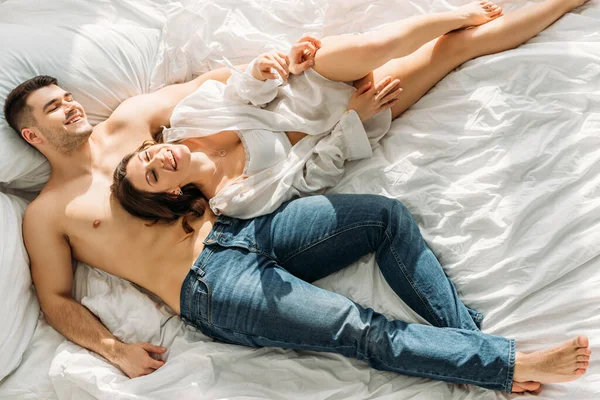 ジーンズ姿のハンサムな若い男と白いシャツ姿のセクシーな女の子がベッドに横になりながら微笑む — ストック写真