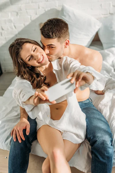 在男朋友亲吻时 快乐女孩在智能手机上自私自利的选择性焦点 — 图库照片