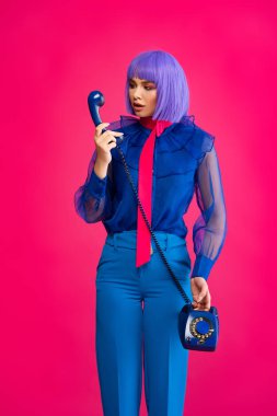 Mor peruklu, modaya uygun bir kız eski telefondan konuşuyor, pembe renkte izole edilmiş.