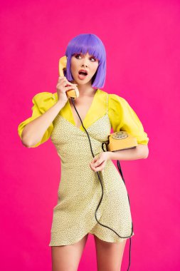 Mor peruklu güzel, şok olmuş kız eski telefondan konuşuyor, pembe renkte izole edilmiş.