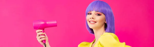 全景拍摄的快乐的流行艺术女孩在紫色假发使用吹风机 孤立在粉红色 — 图库照片