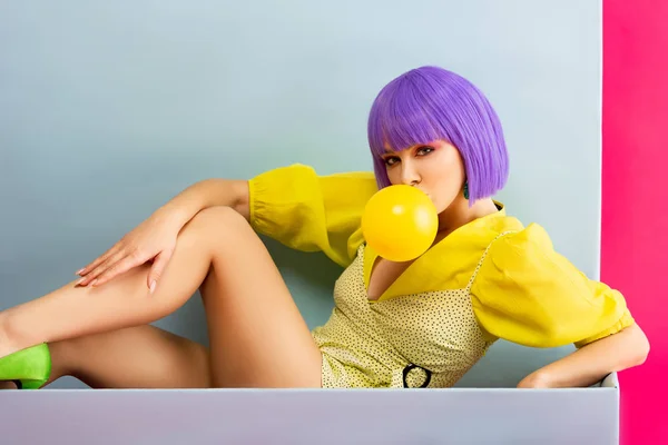 穿着紫色假发的性感女孩 坐在蓝色的盒子里 与粉色隔离 就像玩具娃娃吹泡泡糖 — 图库照片