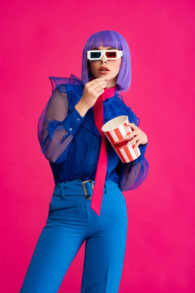 pop art girl in purple wig and 3d glasses eating popcorn, isolated on pink