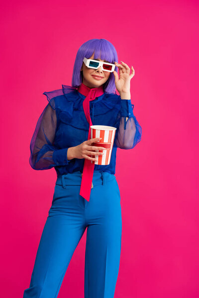 happy pop art girl in purple wig and 3d glasses holding popcorn, isolated on pink