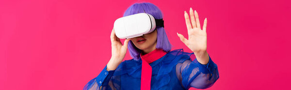 panoramic shot of attractive pop art girl in blue blouse and purple wig using virtual reality headset, isolated on pink