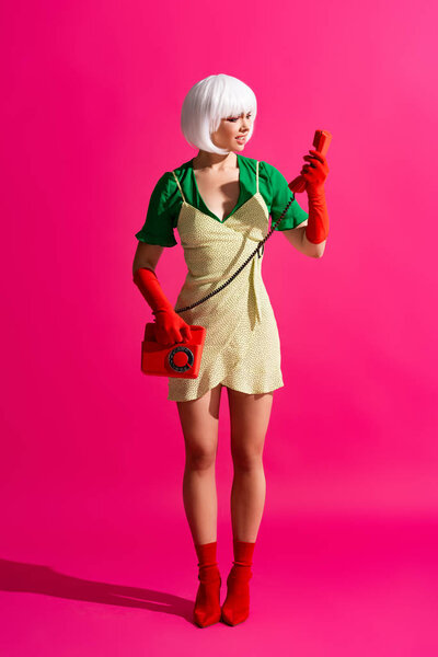 shocked pop art girl in white wig talking on retro telephone, on pink