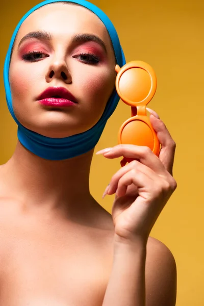 beautiful nude woman in scarf holding sunglasses, on yellow