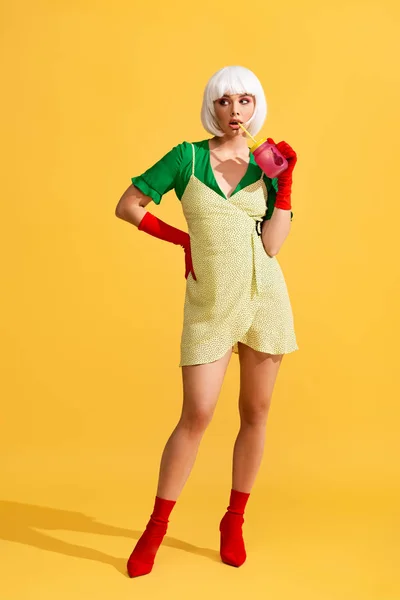 Thoughtful beautiful pop art girl in yellow dress and white wig holding jar with fresh drink, on yellow — Stock Image Thoughtful Beautiful Pop Art Girl Yellow Dress White Wig Holding Stock Photo