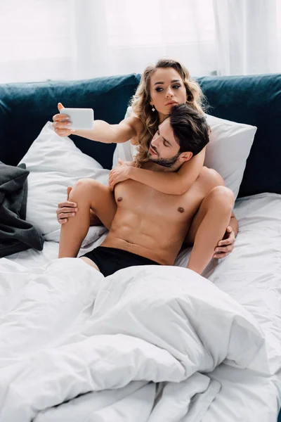 Mulher Atraente Tomando Selfie Com Smartphone Perto Namorado Muscular Cama — Fotografia de Stock