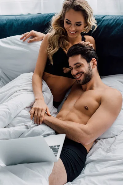 Mujer Sonriente Sujetador Mirando Portátil Cerca Novio Guapo Cama — Foto de Stock