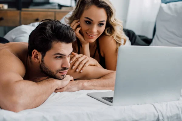 Knappe Man Kijkt Naar Laptop Buurt Glimlachende Vrouw Bed — Stockfoto